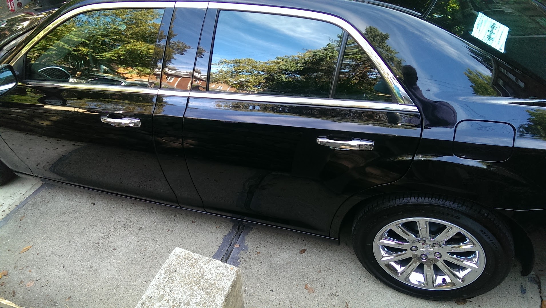 Polished black luxury sedan with chrome wheels parked on a shaded street
