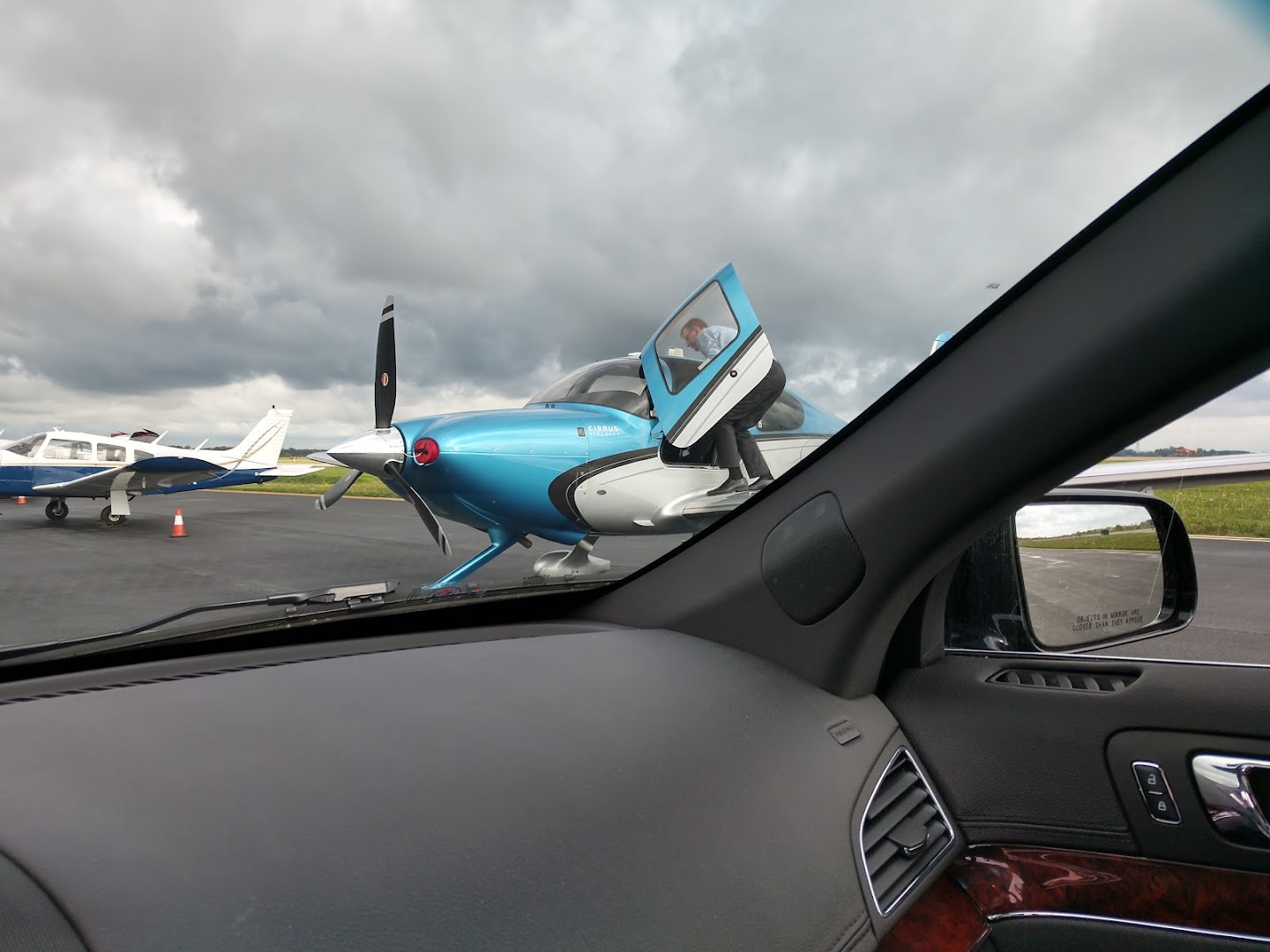 View from inside a luxury sedan toward small private aircraft on a tarmac